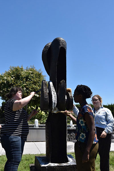 IMLS Conservation Interns, Morgan Shedd, Aleyah Grimes, and Megan Mezera (from left to right), brush-clean Seymour Lipton’s 1966 bronze work, “Oracle.”