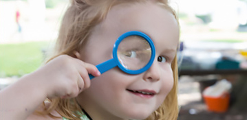 A child with a magnifying lens up to her face